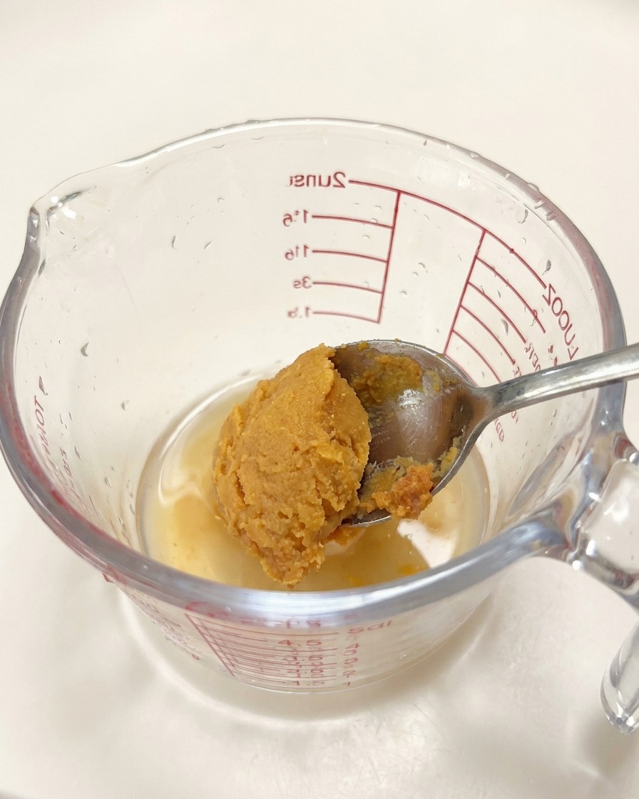 Un cucchiaio di pasta di miso aggiunto a un misurino di vetro con condimenti liquidi.