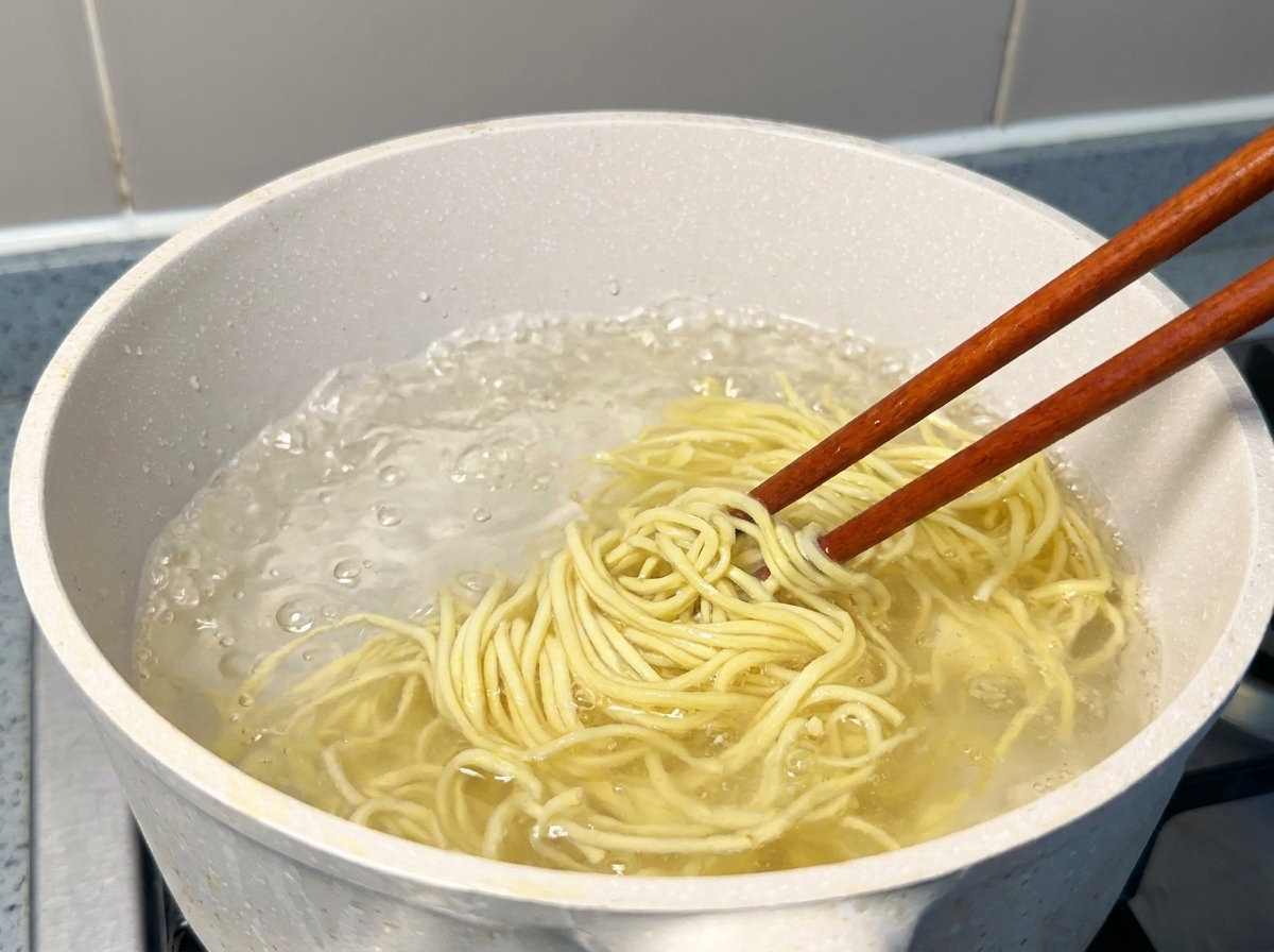 Noodles per ramen freschi e gialli sollevati con bacchette di legno da una pentola dacqua bollente.