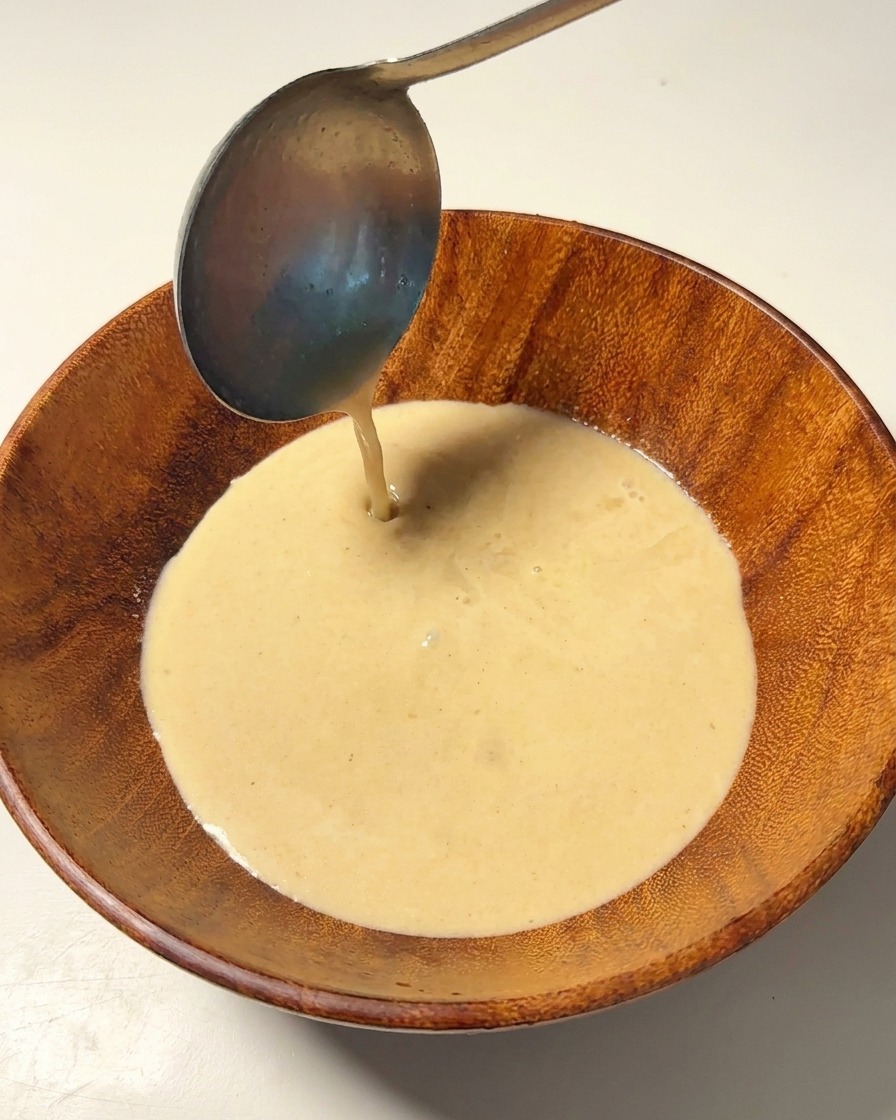 Brodo di ossa di maiale caldo e cremoso versato con un mestolo di metallo in una ciotola di legno.