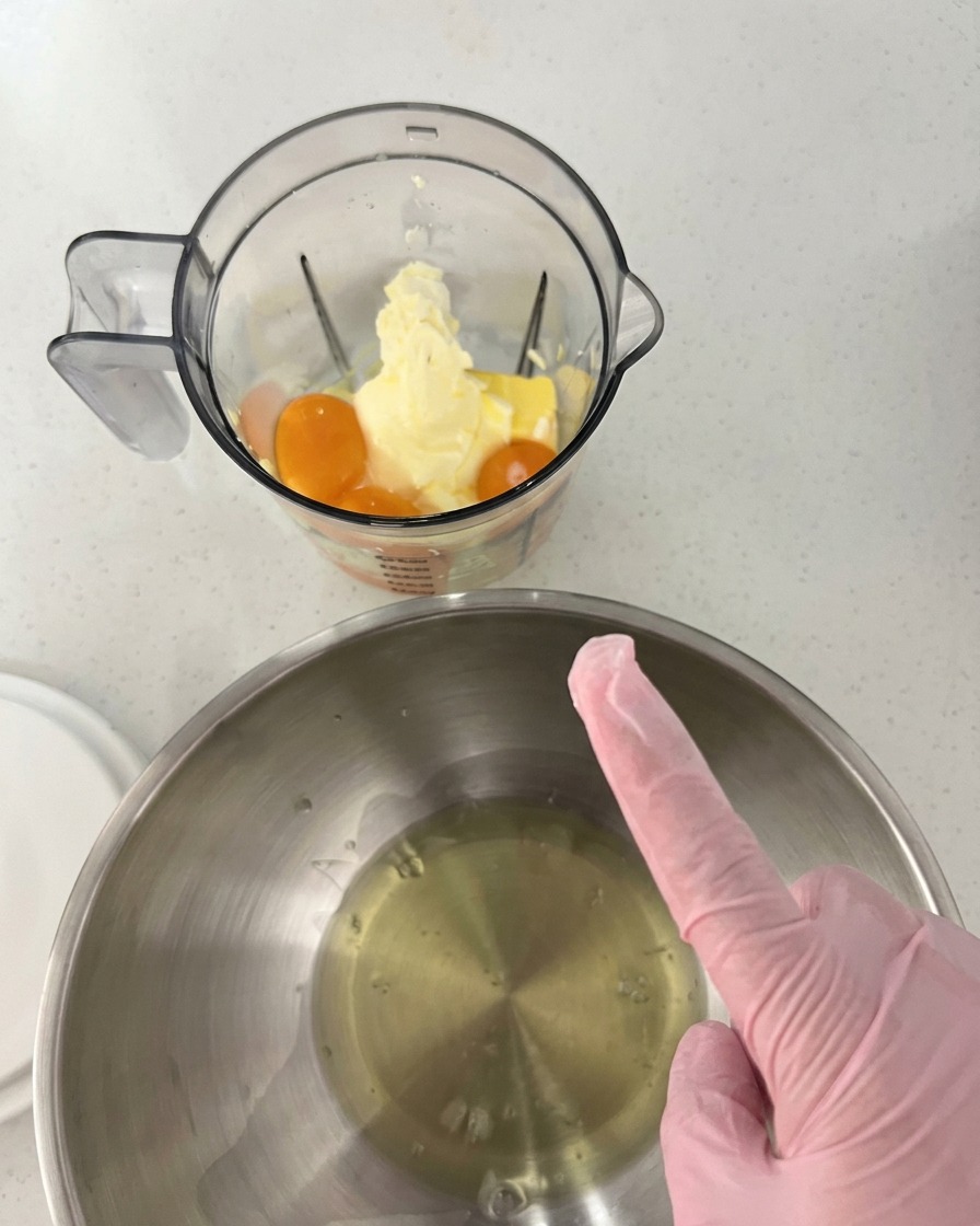 Tuorli, burro e formaggio in un frullatore, accanto a una ciotola in acciaio inox con gli albumi.