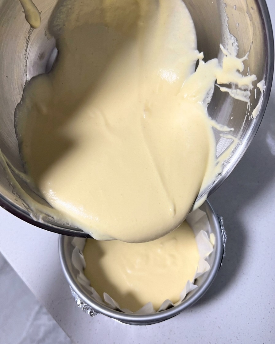 Limpasto liscio della cheesecake viene versato dalla ciotola in uno stampo rotondo da 15 cm foderato con carta forno stropicciata.