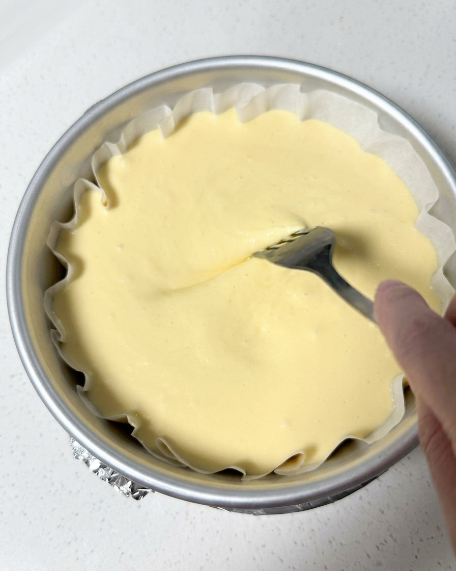 Una mano usa una forchetta di metallo per livellare delicatamente la superficie dellimpasto nello stampo foderato.
