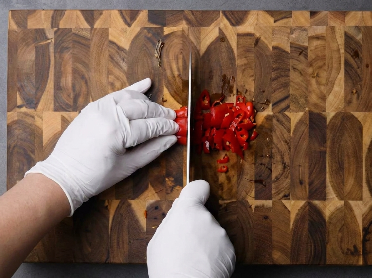 Mani che tritano peperoncini rossi freschi su un tagliere di legno.