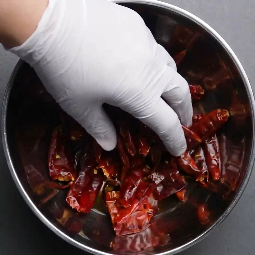 Mano che immerge peperoncini rossi secchi interi in una ciotola dacqua per farli ammollare.