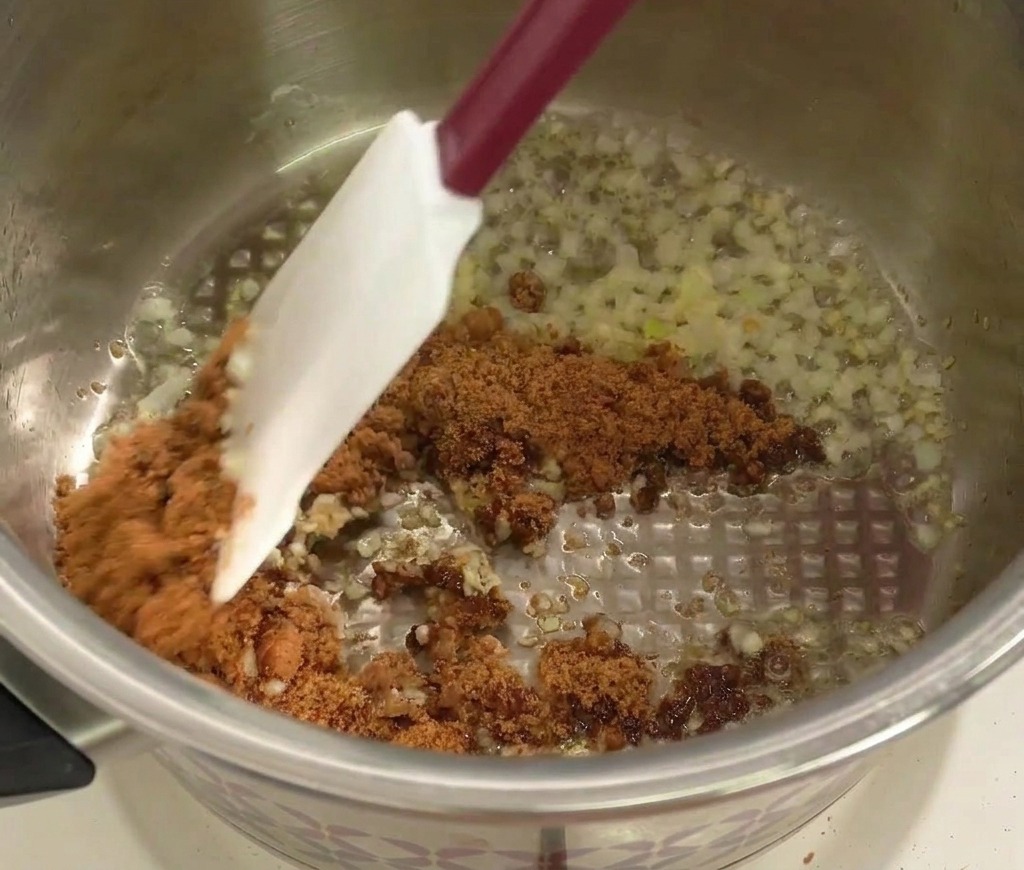 Una spatola mescola lo zucchero di canna scuro al soffritto di cipolla e aglio.