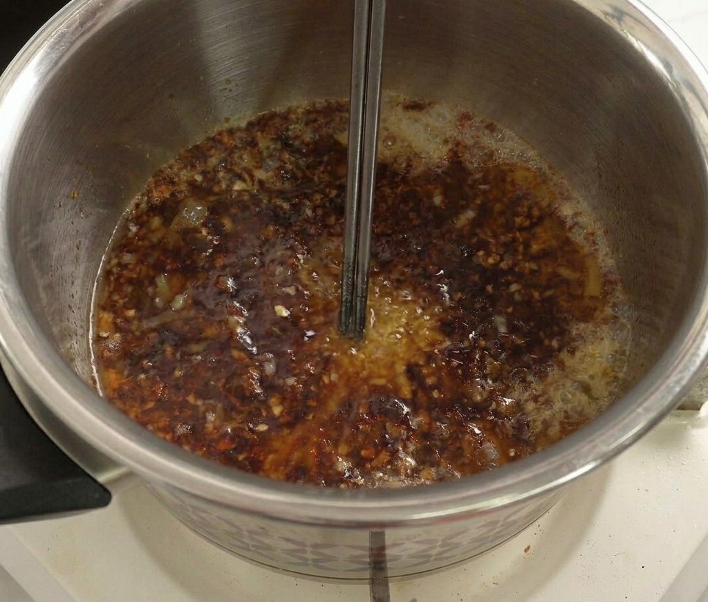 Una miscela liquida e scura che sobbolle in pentola, mescolata con delle bacchette di metallo.