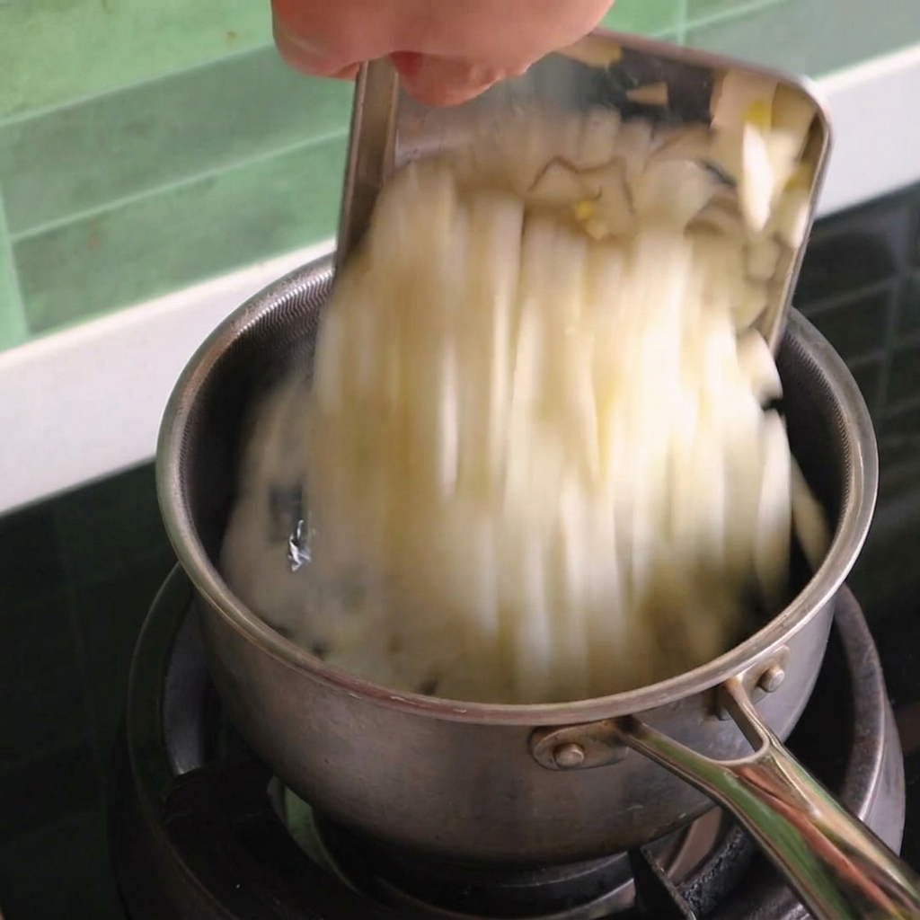 Cipolle bianche a dadini versate in un pentolino di acciaio inossidabile su un fornello a gas.