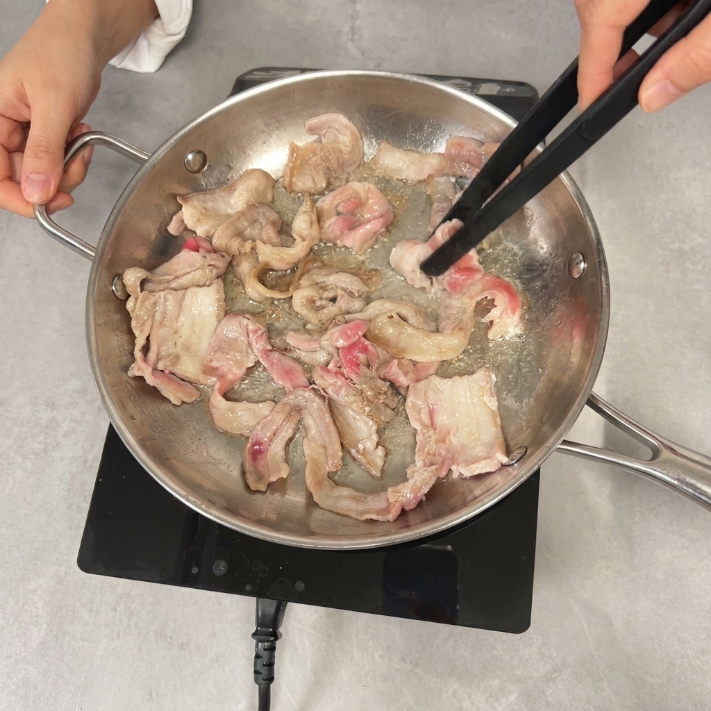 Uso di pinze nere per saltare in padella fette di pancetta di maiale parzialmente rosolate.