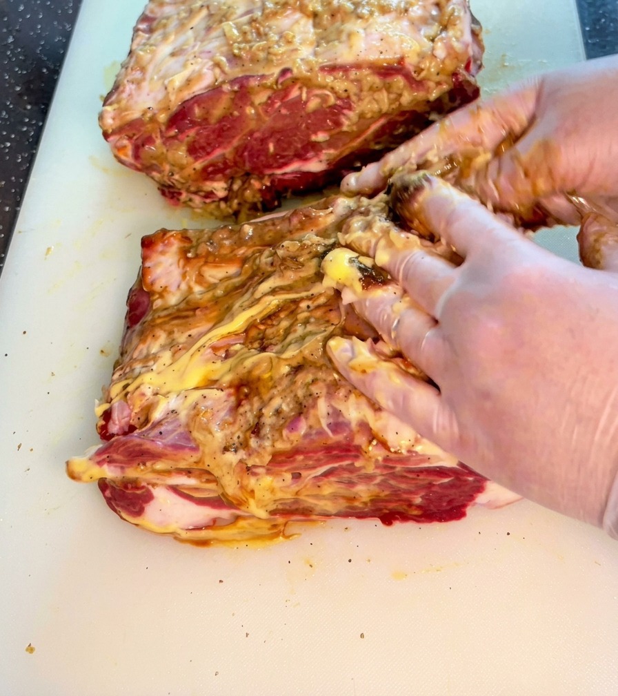 Mani che massaggiano attivamente il mix di salse e spezie su un pezzo di manzo.