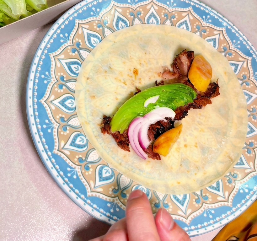 Manzo sfilacciato con avocado e cipolla rossa al centro di una tortilla su un piatto decorato.