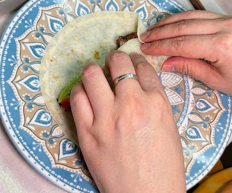 Due mani che arrotolano con cura una tortilla farcita con manzo e verdure.