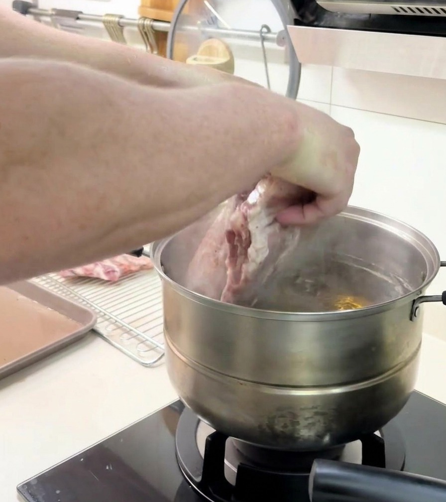 Una persona che usa entrambe le mani per immergere con cura un grande rack di costine in una pentola dacqua fumante.