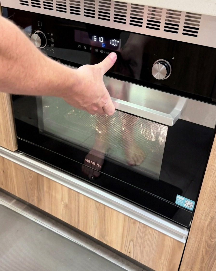 Una mano che preme un pulsante su un moderno pannello digitale del forno impostato a 100 gradi.