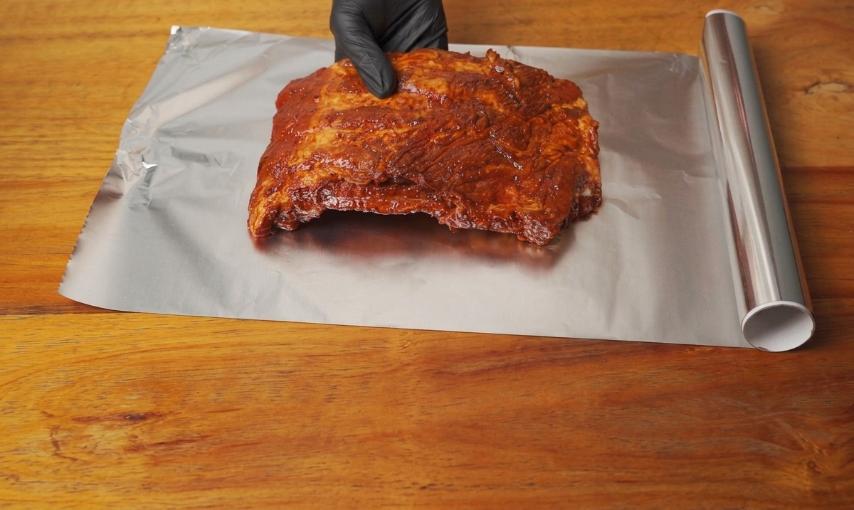 Costine di maiale marinate poste su un foglio di alluminio su un tavolo di legno.
