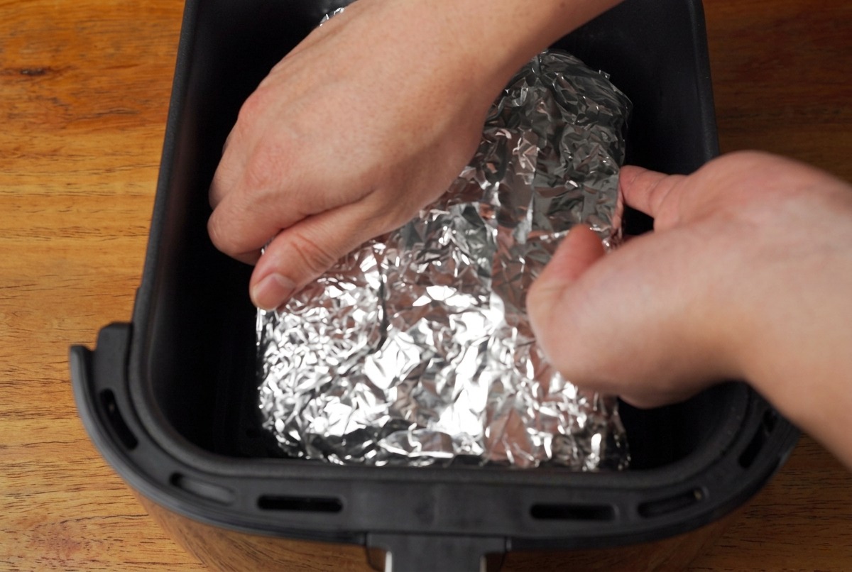 Mani che inseriscono il cartoccio di alluminio con le costine nel cestello della friggitrice ad aria.