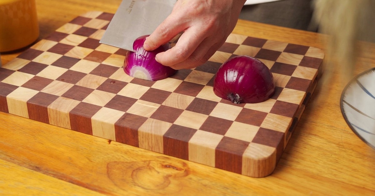 Mani che tritano una cipolla rossa su un tagliere di legno.
