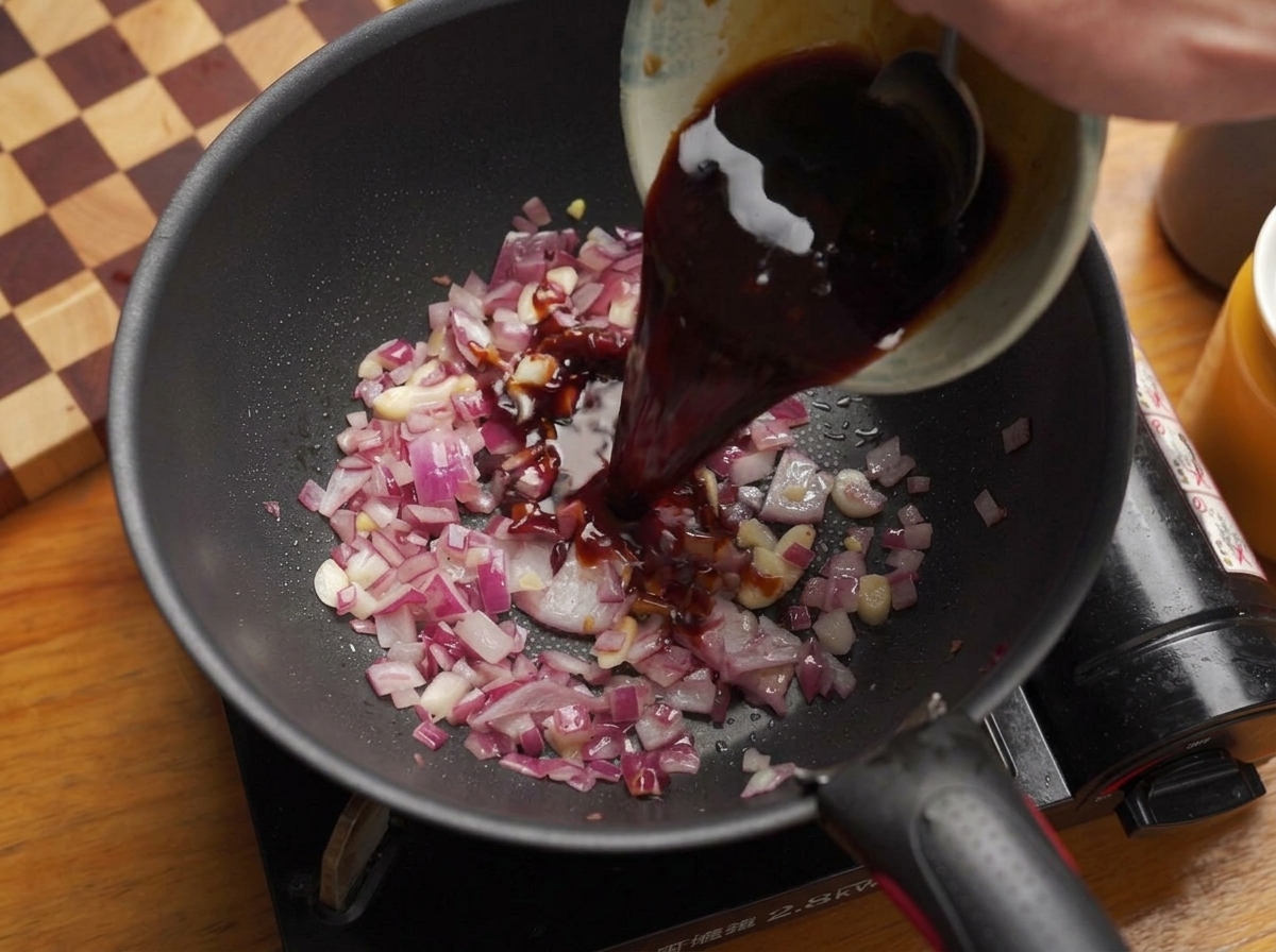Versamento di una salsa barbecue scura in una padella con cipolle e aglio.