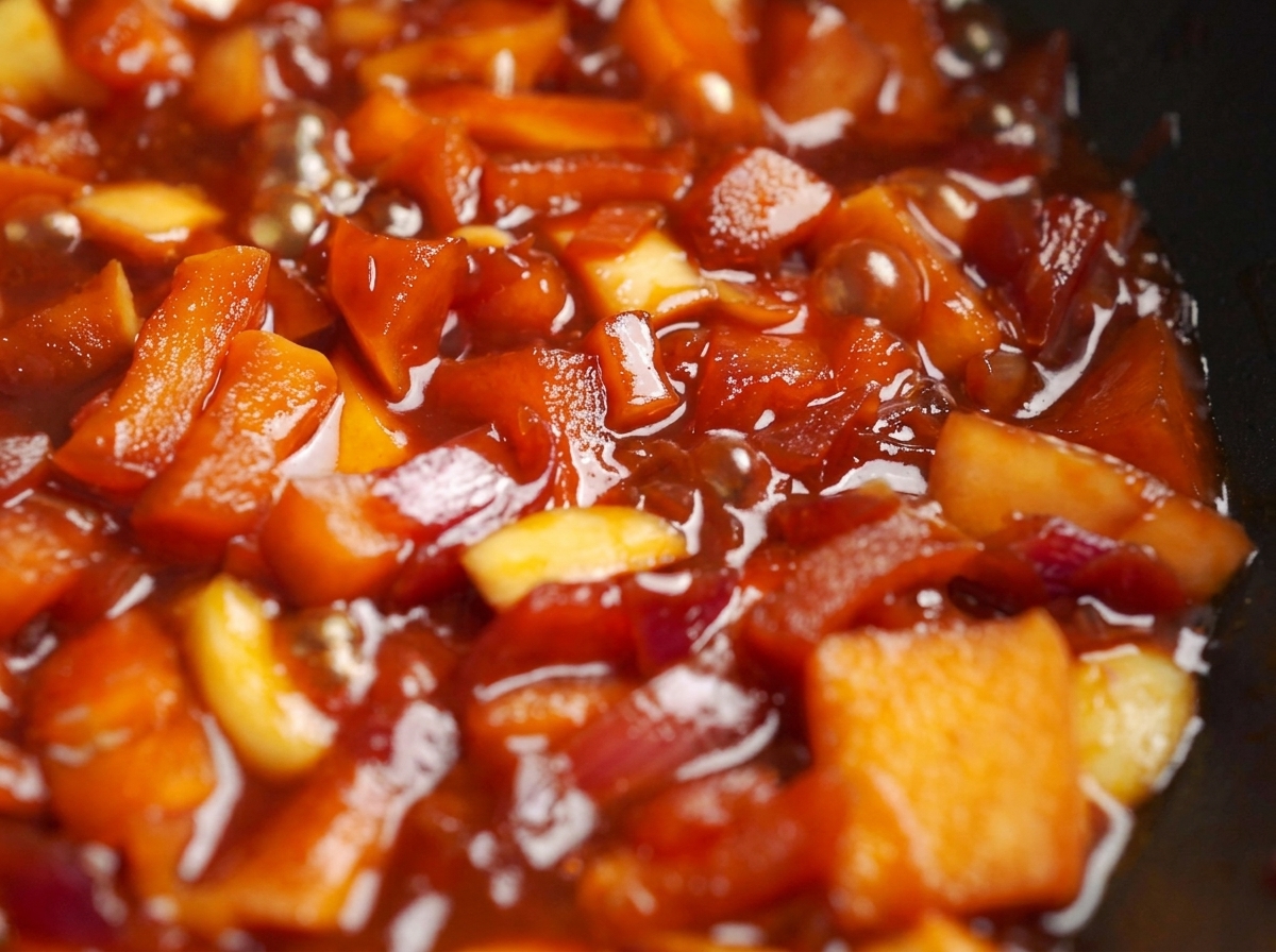 Mele e cipolle che sobbollono in una salsa rossa densa in padella.