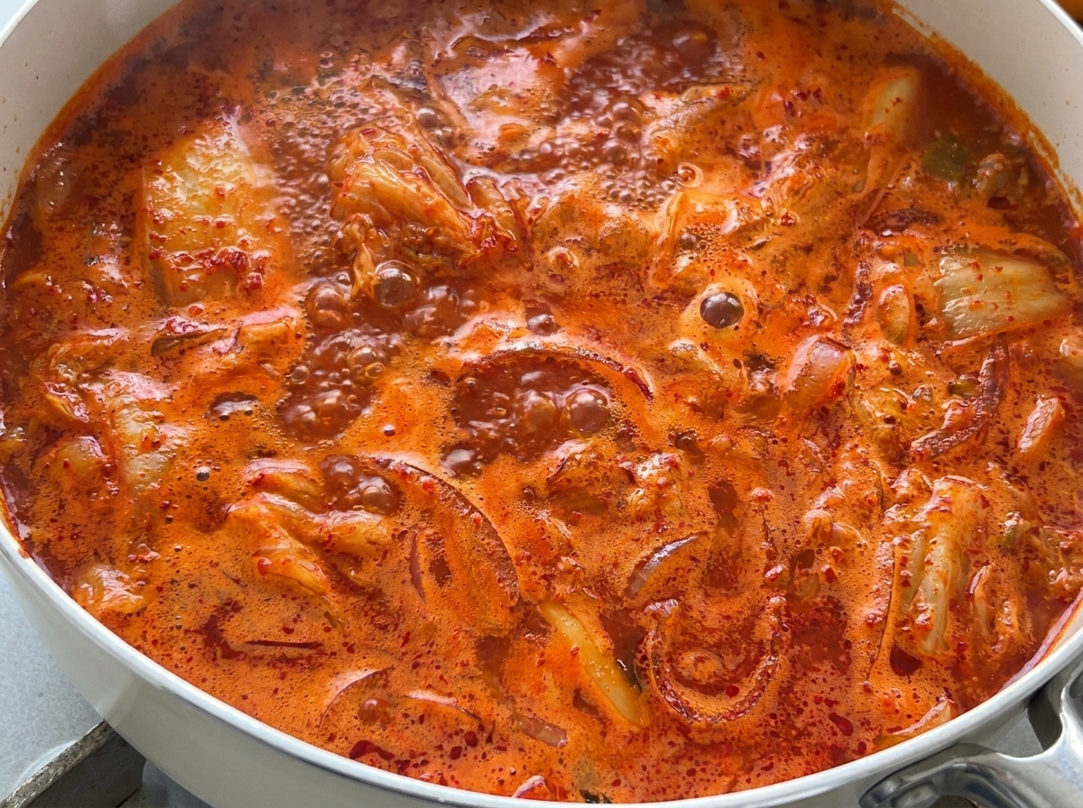Un primo piano della zuppa di kimchi rosso vivo che bolle vigorosamente in padella.