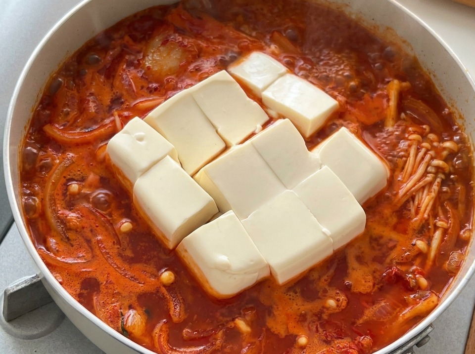 Grandi cubi di tofu bianco e morbido immersi in uno stufato coreano al kimchi caldo e fumante.