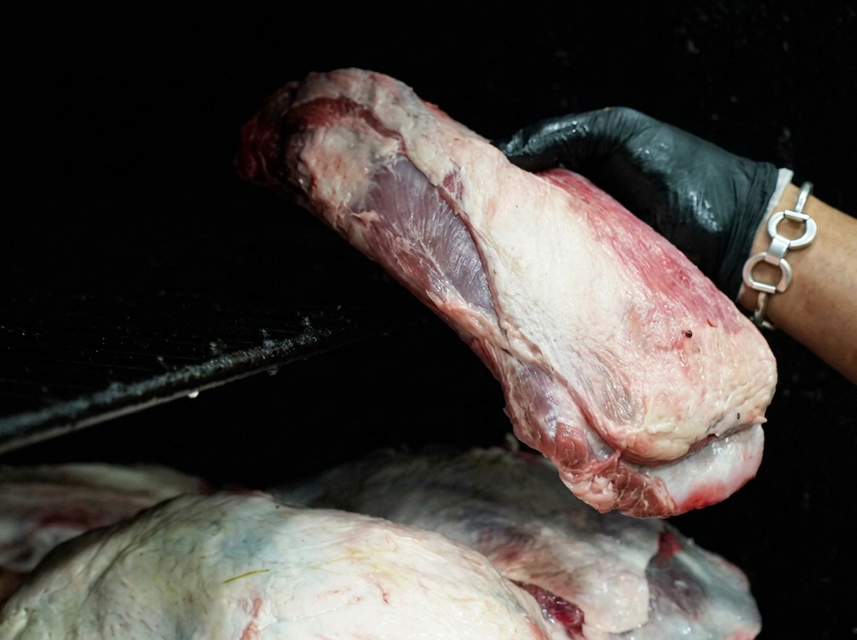 Una mano con guanto nero che posiziona un grosso taglio di manzo crudo sulle griglie di un affumicatore nero.