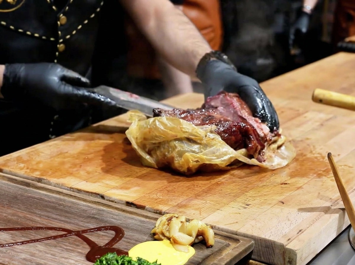 Uno chef che usa un coltello per aprire linvolucro di cottura, rivelando un brisket scuro e succulento su un tagliere di legno.