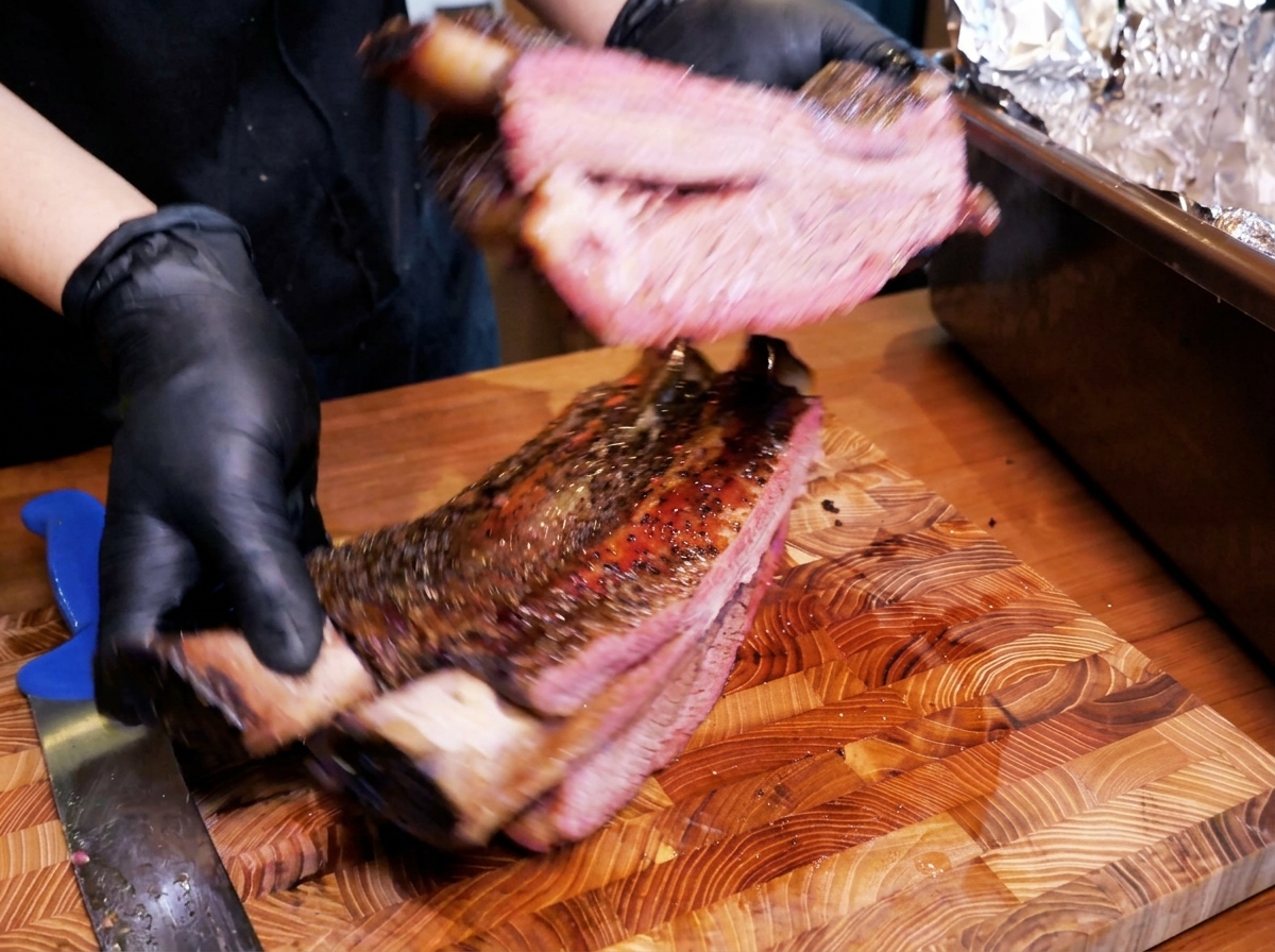 Un grosso rack di costine di manzo affumicate con una crosta scura, che rivela un interno succoso e rosato.