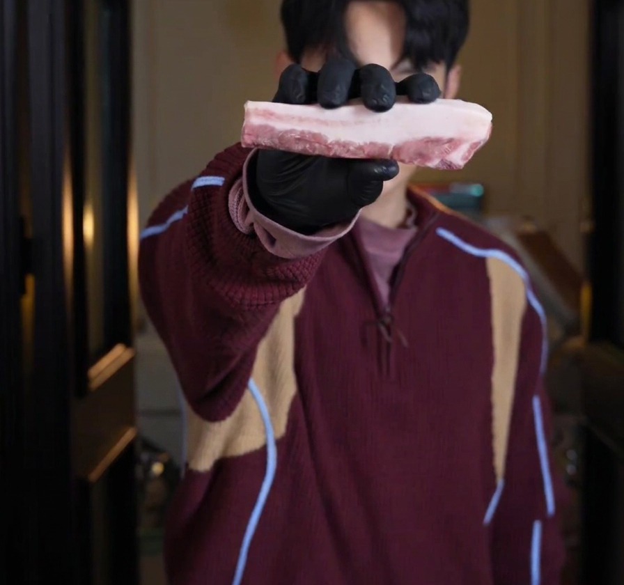 Una persona con guanti neri tiene in mano un pezzo spesso di pancetta di maiale cruda con strati ben visibili.