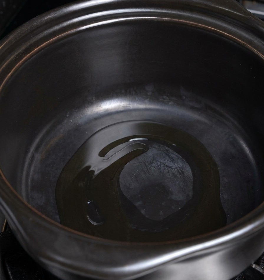 Un sottile strato di olio di cottura che luccica sul fondo di una pentola in ceramica scura riscaldata.