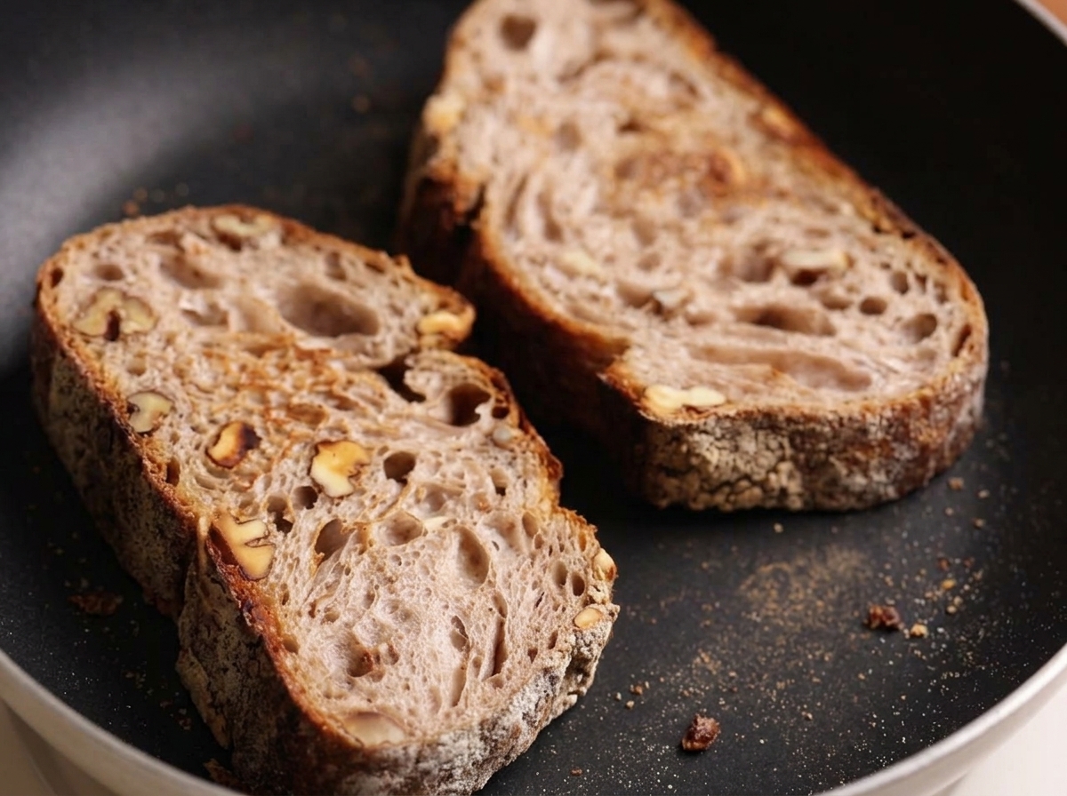 Due fette di pane rustico che tostano in una padella piatta.