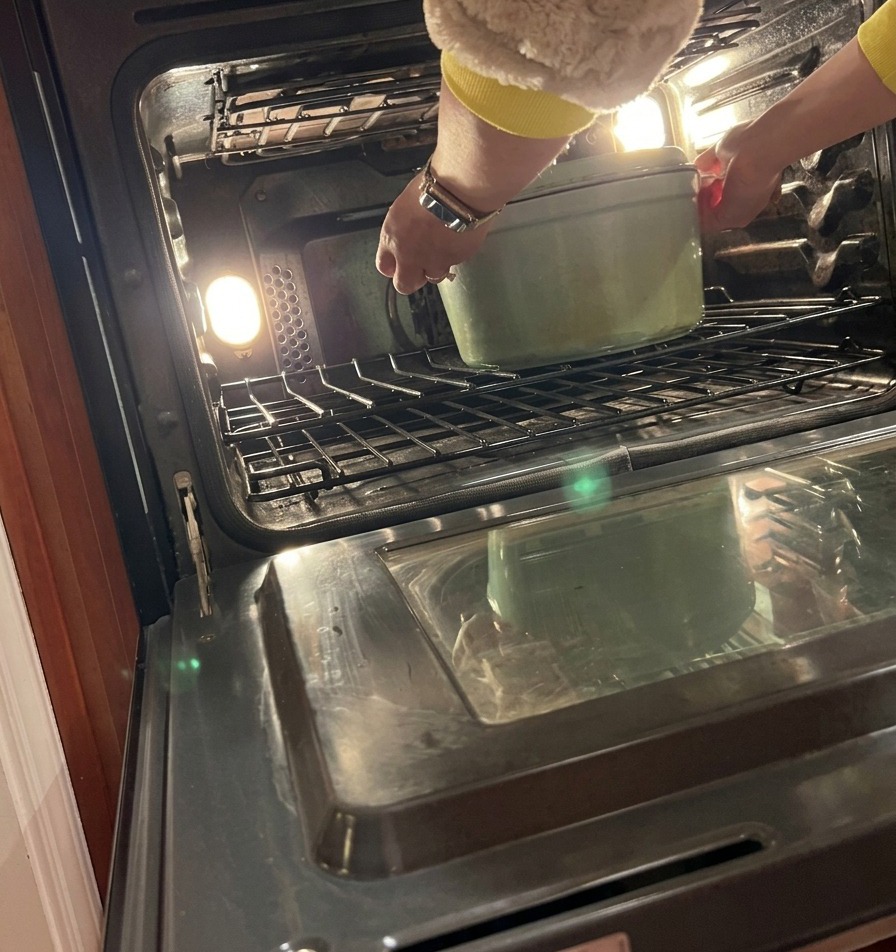 Una persona mette con cura una cocotte in ghisa coperta sul ripiano centrale di un forno preriscaldato.