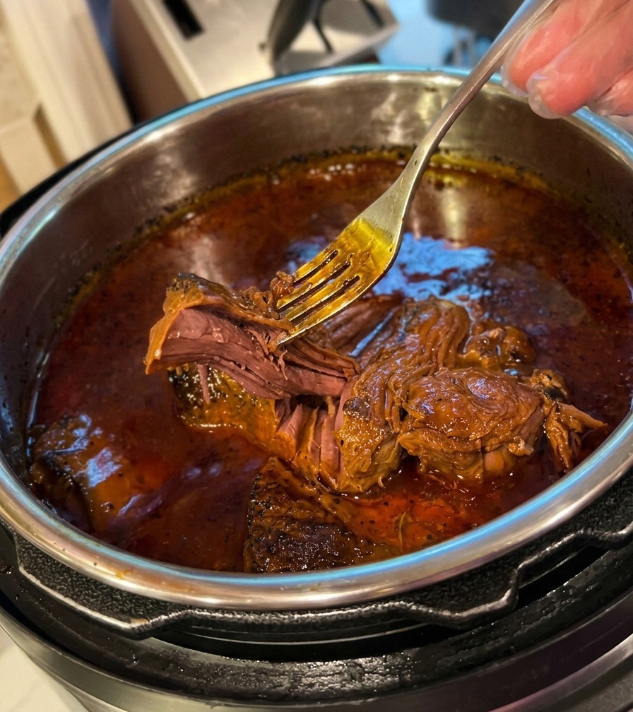 Una forchetta in metallo sfilaccia facilmente del manzo tenerissimo immerso in un fondo di cottura scuro.