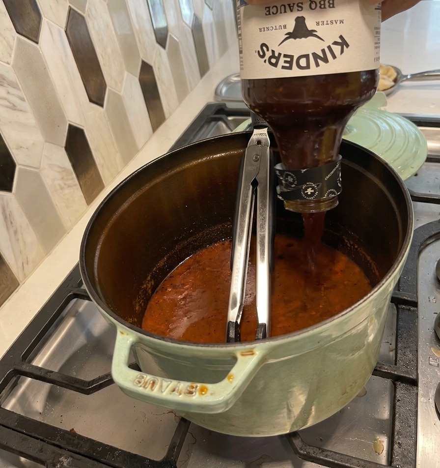 Salsa barbecue versata in una pentola verde piena di un liquido scuro e ristretto.