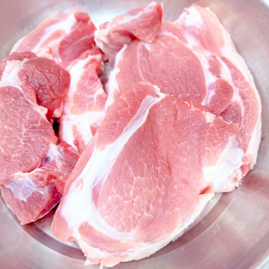 Tagli spessi di spalla di maiale cruda posti in una ciotola di acciaio inox.
