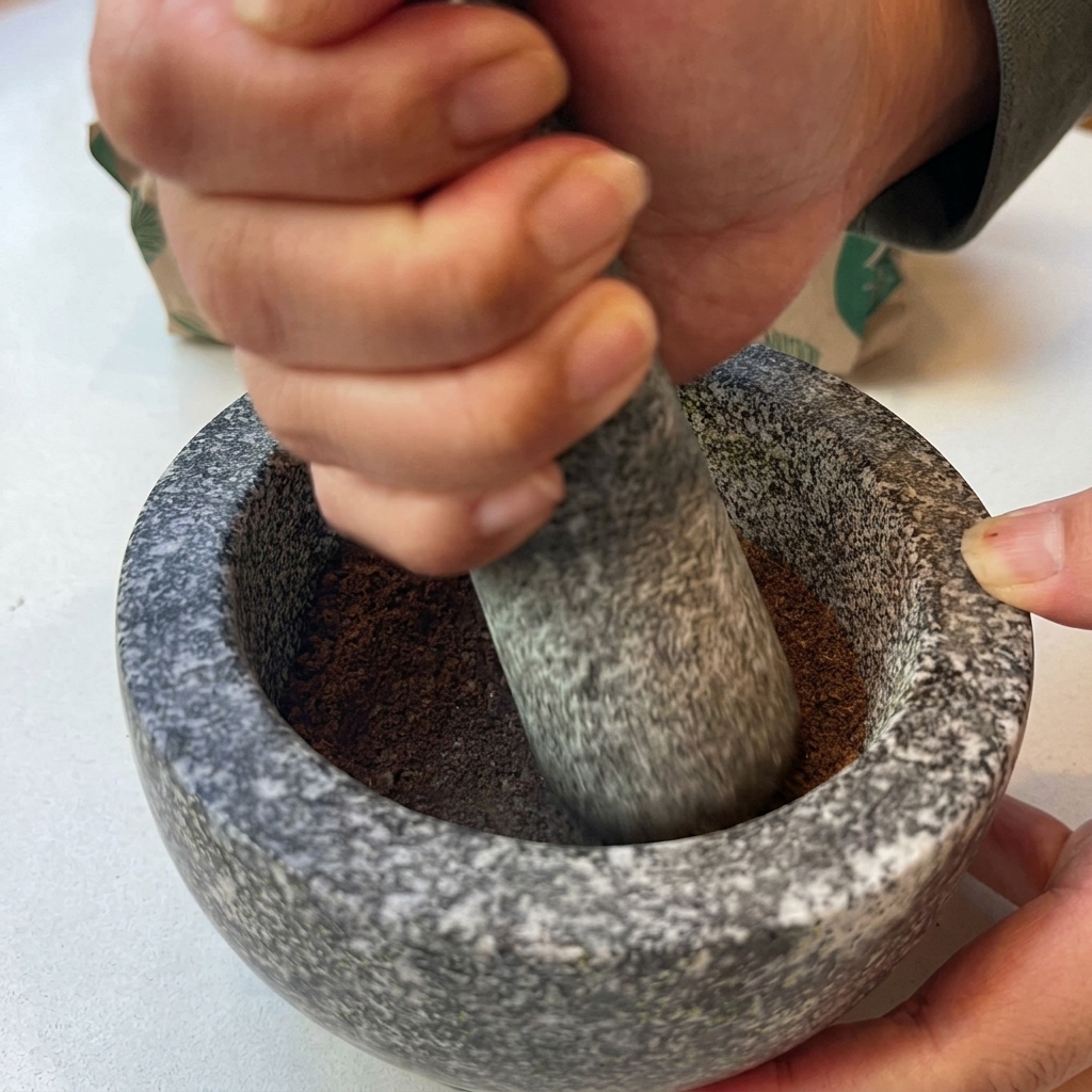 Un paio di mani che usano un pestello di pietra per macinare le spezie tostate in una polvere fine allinterno di un mortaio di granito.