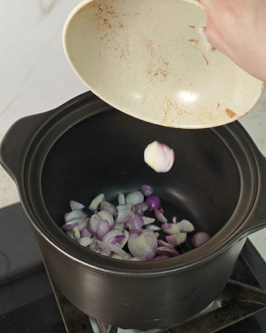 Fette di scalogno rosso versate da una ciotola sul fondo di una pentola di ceramica scura.