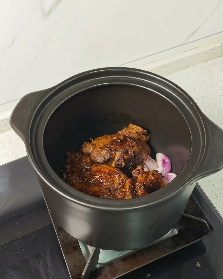 Pezzi di maiale ben rosolati adagiati sopra gli scalogni affettati in una pentola di ceramica.
