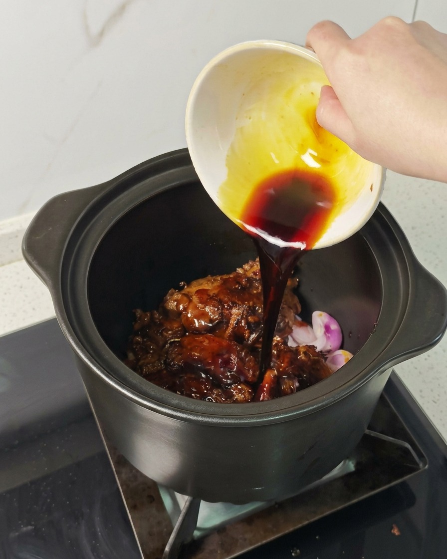 Una mano versa una salsa scura e saporita da una ciotolina sul maiale rosolato nella pentola.