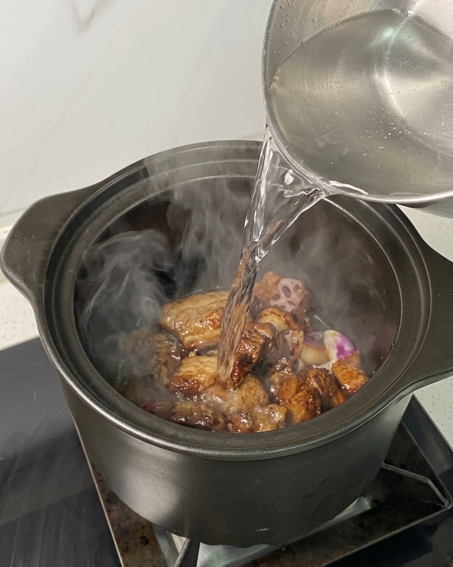 Acqua bollente versata da un bollitore sopra il maiale e gli scalogni in pentola.