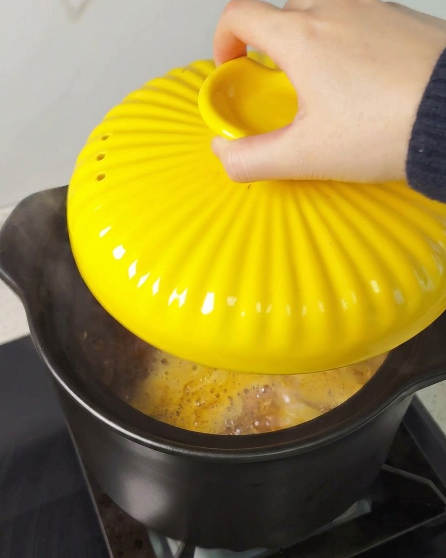 Una mano posiziona un coperchio giallo scanalato su una pentola nera sul fornello.