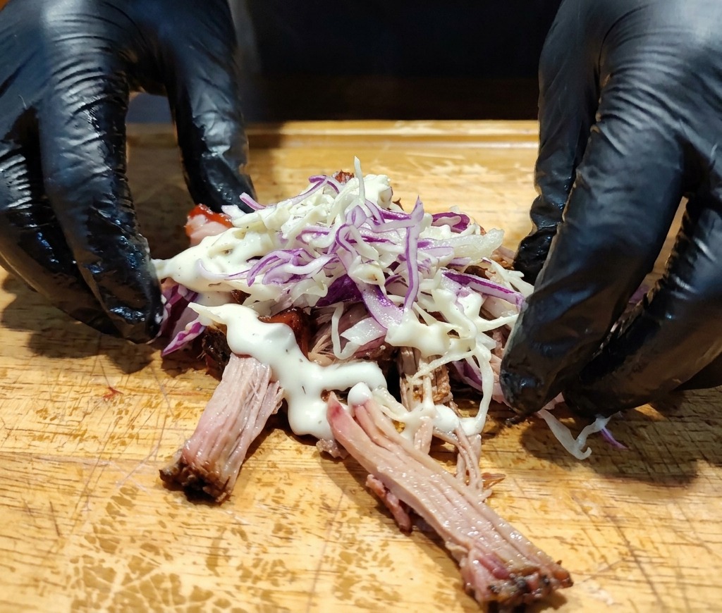 Mani accanto a un mucchietto di pulled pork guarnito con cavolo e una crema bianca densa.