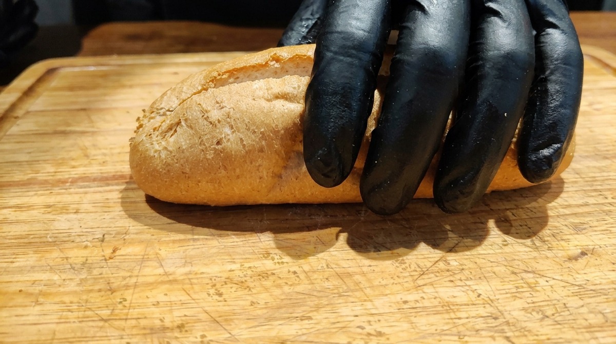 Mano che appoggia una baguette integrale parzialmente tagliata su un tagliere.