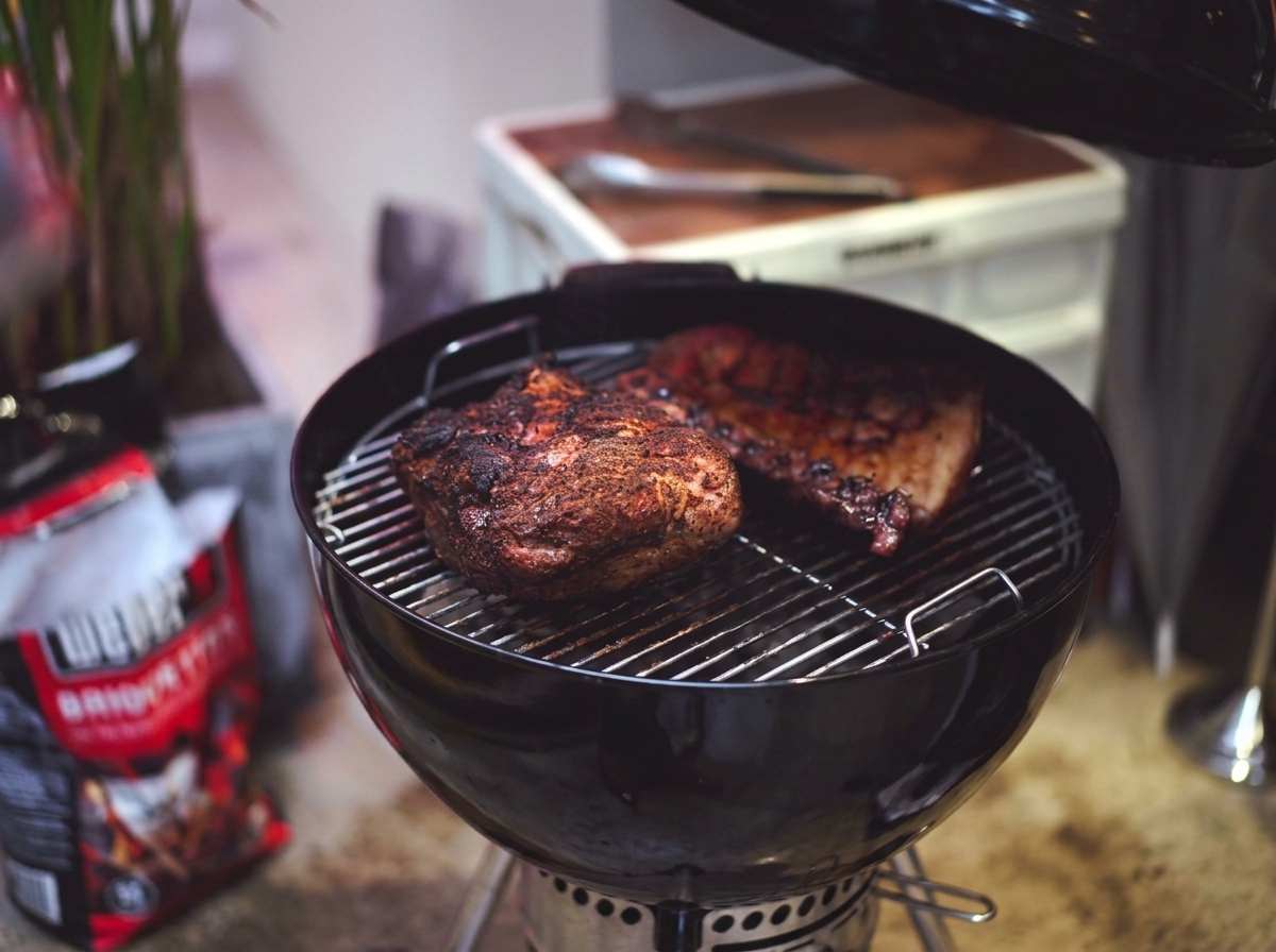 Spalla di maiale e costine parzialmente cotte con una crosta scura caramellata sulla griglia del barbecue.
