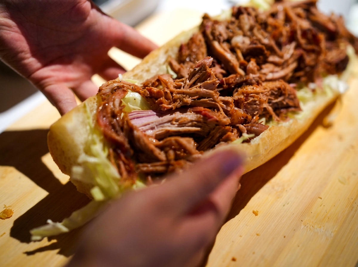 Mani che tengono con cura un panino lungo generosamente farcito con coleslaw cremosa e pulled pork caldo e succoso.