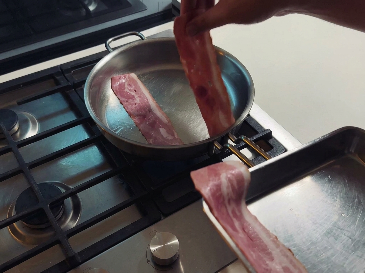 Due strisce di bacon che friggono in una padella di acciaio rilasciando il loro grasso naturale.