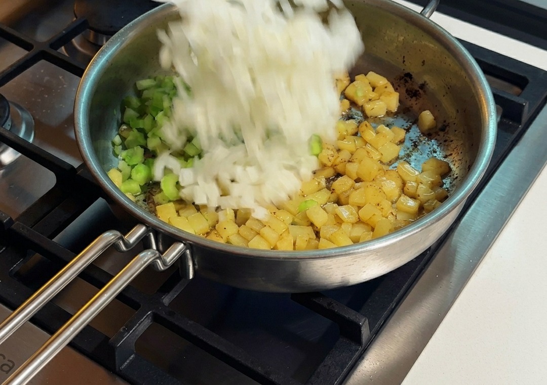 Cipolla bianca tritata aggiunta da un piatto bianco in una padella con sedano e patate dorate.
