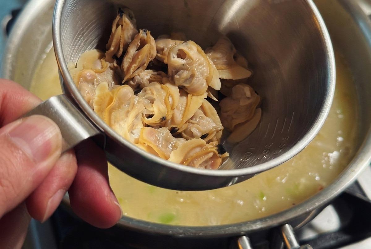 Panna fresca versata nella pentola di zuppa densa mentre la polpa delle vongole viene aggiunta delicatamente.
