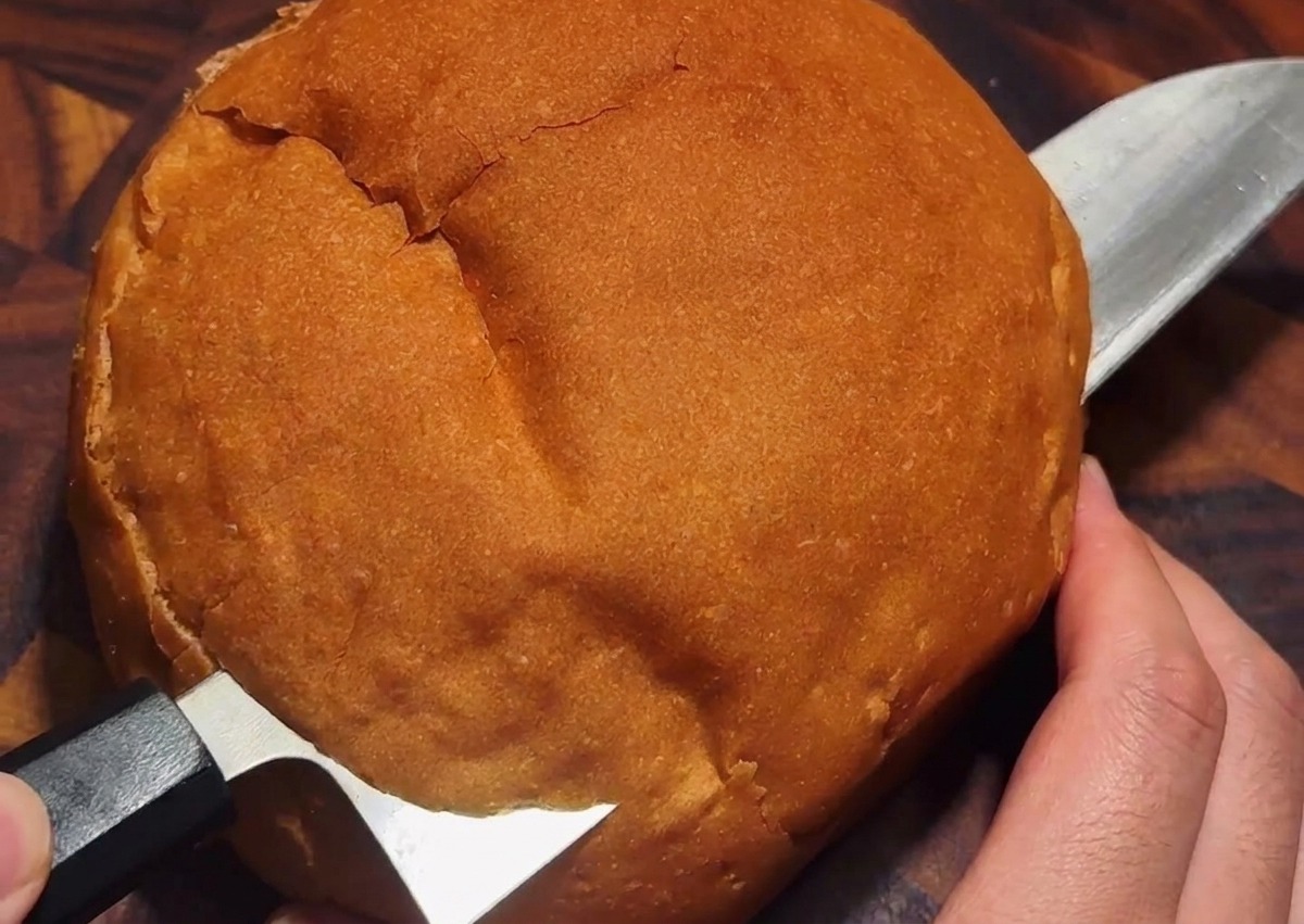 Un coltello che taglia un coperchio circolare sulla crosta di una pagnotta di pane rotonda su un piano di legno.