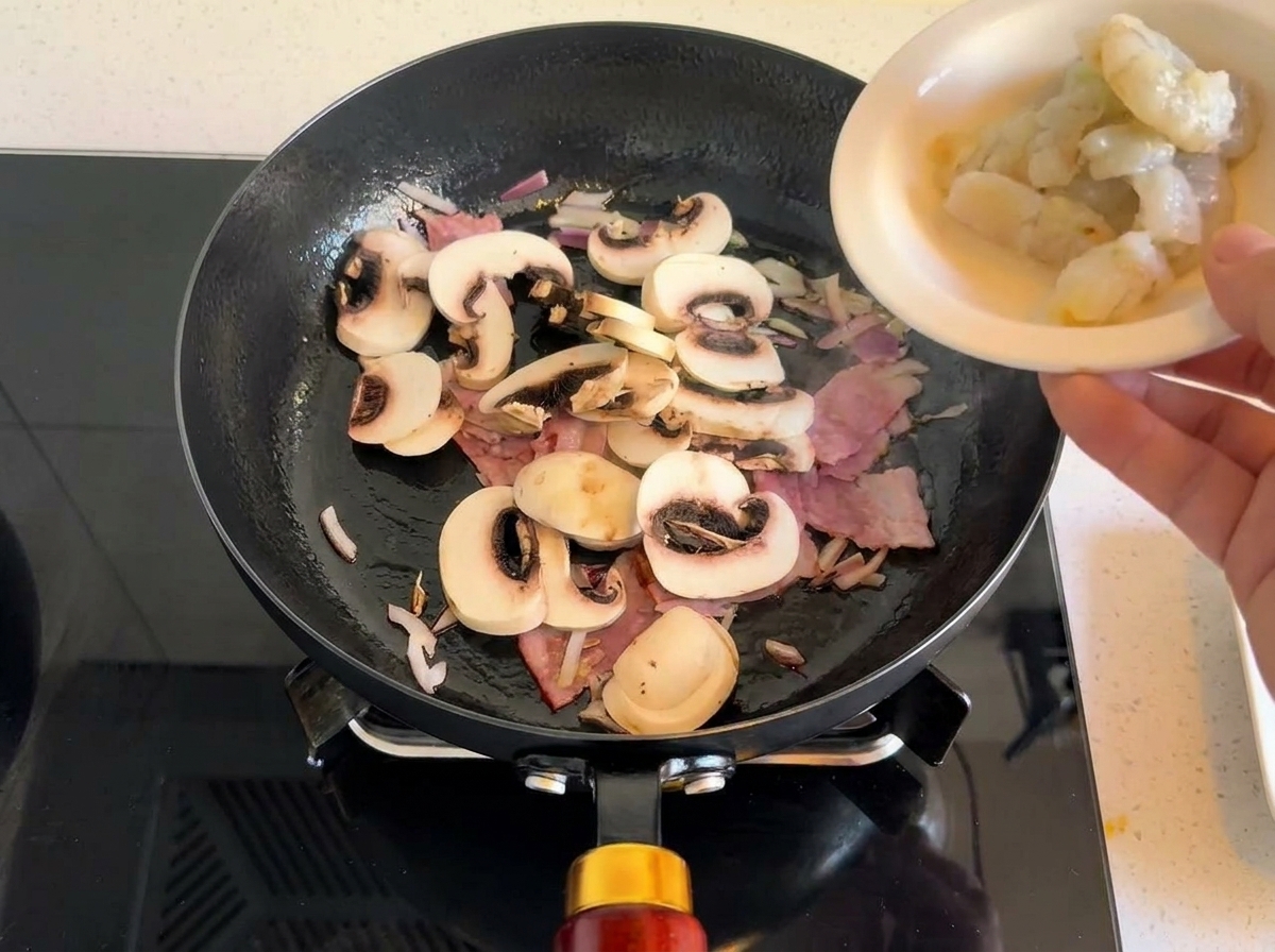 Gamberi crudi aggiunti in padella con pancetta, funghi e cipolle.