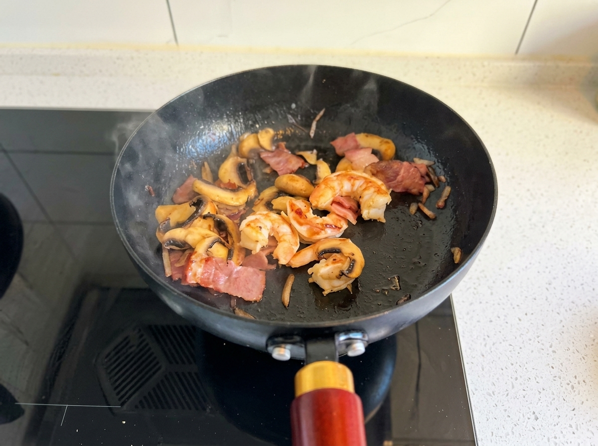 Gamberi, pancetta e funghi saltati in una padella nera finché i gamberi non sono cotti.